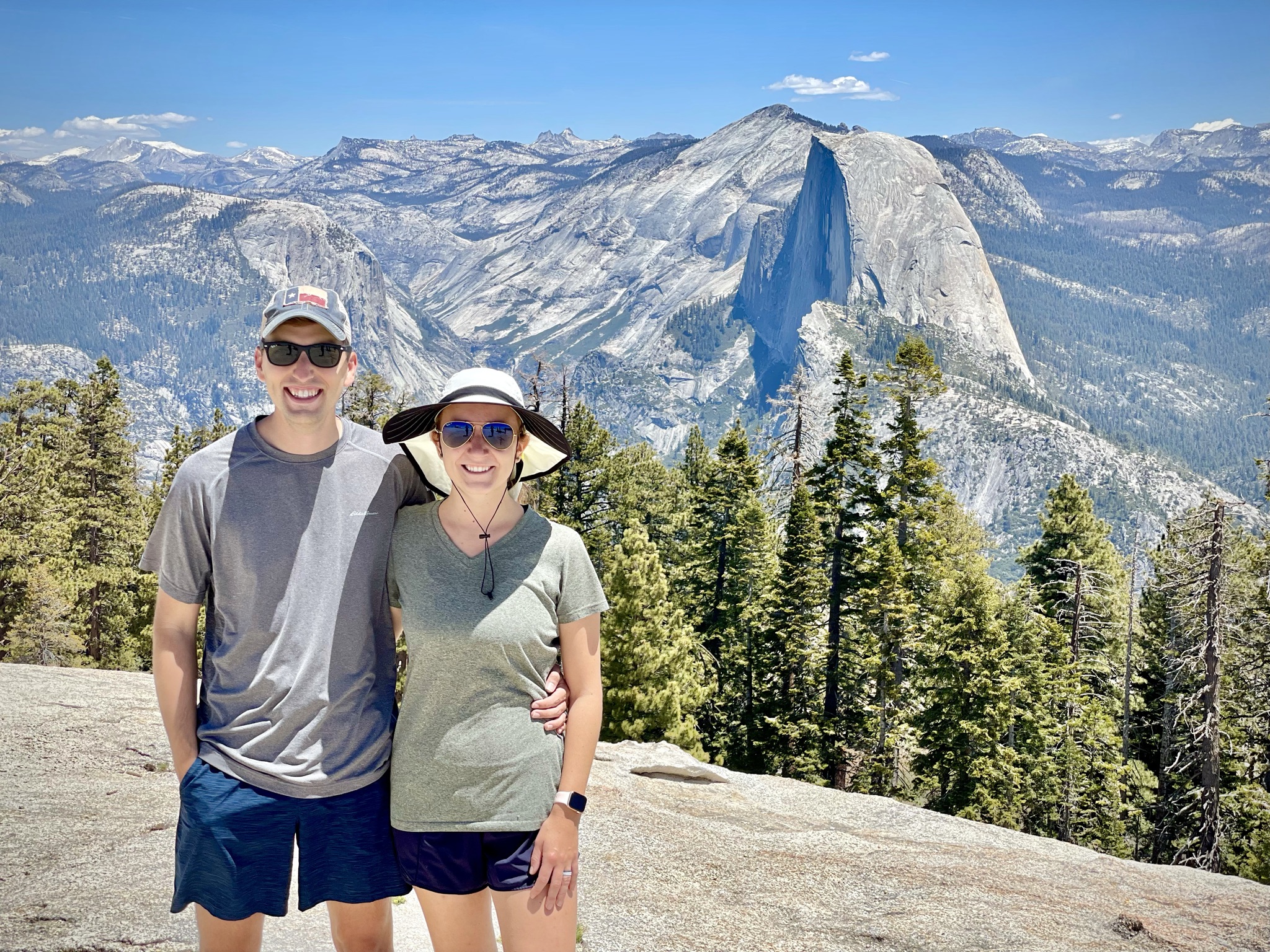 A couple standing at a Yosemite overlook with Half Dome and the surrounding mountains behind them